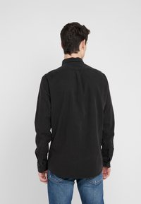 Czarna koszula na długi rękaw zapinana na guziki, z prostym dołem, miękką fakturą i mankietami na pojedynczy guzik, zestawiona z niebieskimi dżinsami.