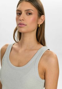 Helehall ribaneelne tank top laiad õlapaelad ja ümmargune kaelus, pehme tekstuur ja ühtlane siluett. Näha on kuldne rõngaskõrvarõngas.