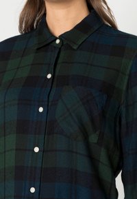 Karierte Herrenhemd aus dunkelgrünem, blauem und schwarzem Flanell. Verfügt über eine Knopfleiste, eine einzelne Brusttasche und ein klassisches Kragendesign.