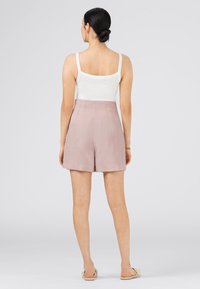 Kevyt, vaaleanpunainen pellavashortsit korkealla vyötäröllä, sileä pinta ja sivutaskut. Yhdistetty tiukkaan valkoiseen hihattomaan pikkutoppioon.