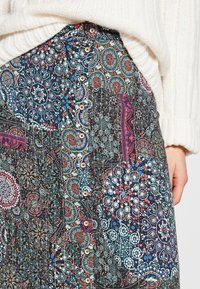 Jupe à motifs présentant des designs complexes dans des teintes de bleu, rouge et blanc. Boutons le long de la taille et un tissu texturé avec des motifs variés.