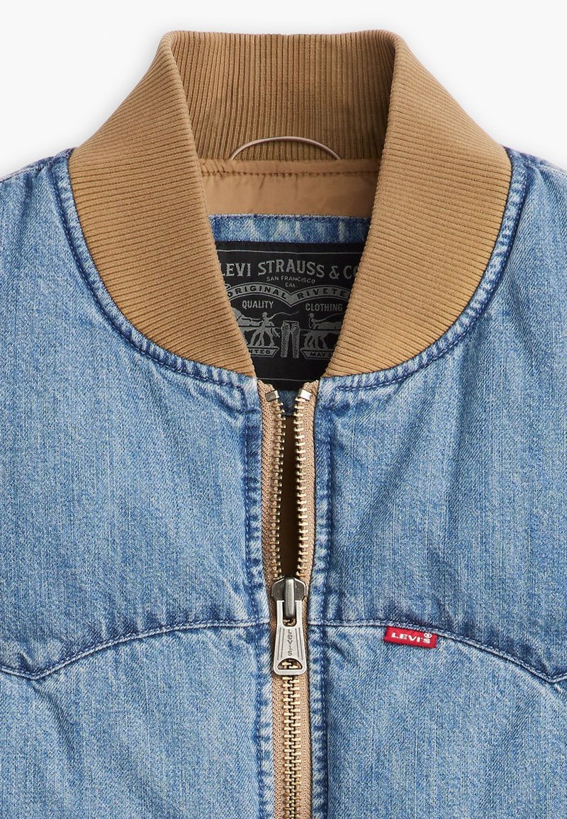 Veste en denim avec un col côtelé marron, fermeture éclair à l'avant et étiquette rouge Levi's. Présente un tissu bleu légèrement texturé et un design classique.