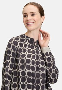 Cotton top featuring a round neckline, dark circular polka dot patterns on a light background, and a button detail at the collar.