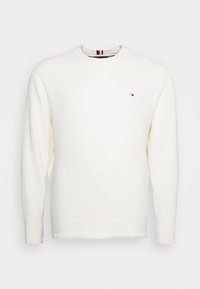 Sweatshirt bianco a maniche lunghe in maglia con colletto rotondo, caratterizzato da un piccolo logo rosso, bianco e blu sul petto e polsini a coste.