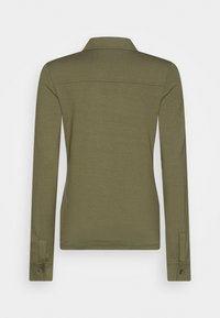 Polo de manga larga en verde oliva con cuello, con corte recto, puños abotonados y una tela suave y texturada.