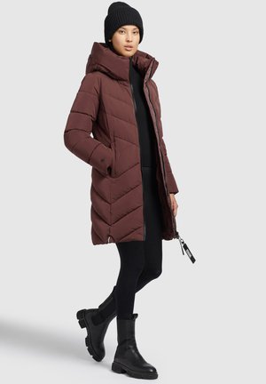 Giacca a vento bordeaux con cappuccio, caratterizzata da un design trapuntato a zigzag, due tasche laterali e una cerniera frontale. Leggings neri e stivali alla caviglia.