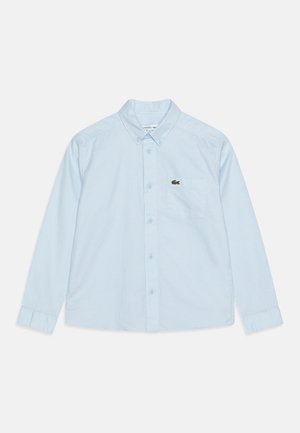 Jasnoniebieska koszula na długi rękaw z guzikami zapinana z przodu, z kieszenią na piersi ozdobioną małym zielonym logo krokodyla.