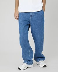 Jean en denim bleu à coupe décontractée avec un design classique, présentant des poches latérales et des coutures visibles, associés à des chaussures de sport blanches.