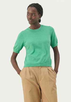 Short-sleeve green knit sweater with a crew neckline, ribbed hem, and slightly puffed sleeves, paired with beige pleated trousers.