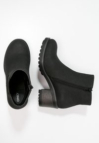 Botas negras hasta el tobillo con un acabado texturizado, cremallera lateral y un tacón cuadrado. Material suave y diseño de puntera redondeada. Detalle en el tacón de contraste.