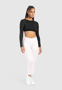 Zwart lange mouwen crop top gecombineerd met lichtroze high-waisted leggings en witte sneakers. Glad materiaal, aansluitend ontwerp.