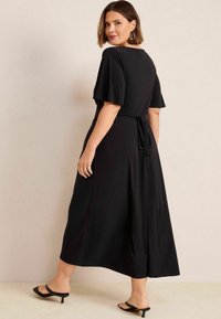 Robe maxi noire avec des manches courtes et flottantes, une taille à nouer et une silhouette fluide. Tissu doux avec un léger brillant, design longueur cheville.