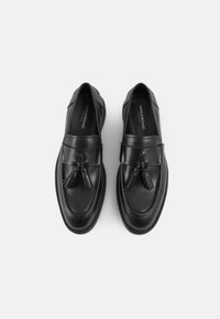 Loafers din piele neagră cu accente din ciucuri, textură netedă, vârf rotund și cusături detaliate. Sunt dotate cu o talpă plată și o însoletrare cu marcă.