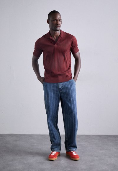 Polo à rayures bourgogne avec col, associé à un jean bleu clair à rayures et des baskets rouges avec des lacets blancs.