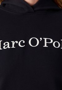 Granatowa bluza z kapturem z białym napisem "Marc O'Pol" z przodu, wykonana z miękkiego, teksturowanego materiału i o luźnym kroju.