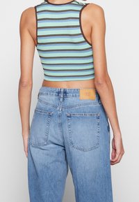 Kort topp med horisontella blå och gröna ränder, ribbad textur och bruna detaljer; kombinerad med ljusblå vida jeans med bakfickor.