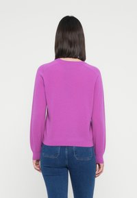 Lilla genser med lange ermer og rund hals, laget av et mykt, teksturert stoff; parret med tettsittende blå jeans.