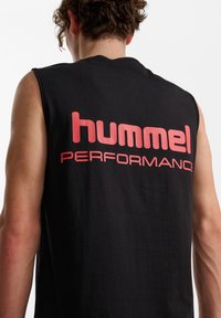 Svart ärmlös t-shirt med stor röd text "hummel PERFORMANCE" på baksidan. Mjukt tyg med avslappnad passform och rundad halsringning.