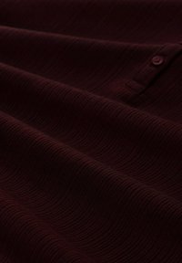 Bordeaux gekleed stof met een golfpatroon en knoopdetail, dat gladde, vloeiende drapes en een rijke kleurdiepte toont.
