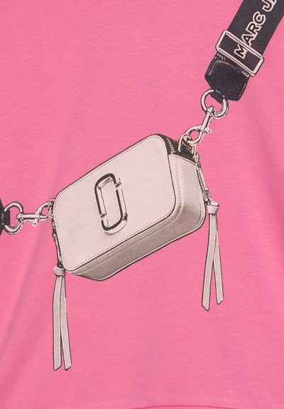 Borsa rettangolare bianca con una cerniera nera e frangette di pelle, attaccata a una tracolla nera con la scritta "MARC JACOBS" in bianco, su uno sfondo rosa.