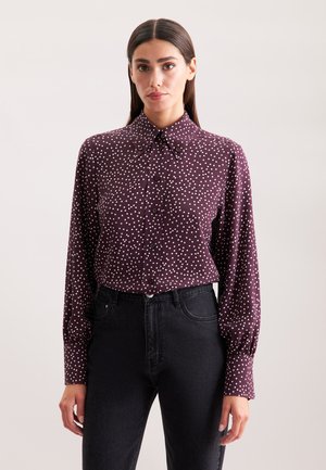 Camicia button-up bordeaux con pois bianchi, colletto a punta e maniche lunghe. Indossata con jeans neri a vita alta.
