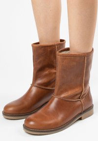 Bruine leren enkellaarsjes met een zachte binnenkant, ronde neus en decoratieve stiksels. De buitenkant heeft een lichte glans en een gevouwen kraag.