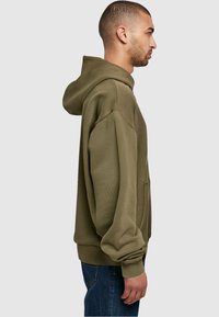 Olive green hooded sweatshirt with a soft texture, oversized fit, and ribbed cuffs. Features a front pocket and a ventilated hood.
