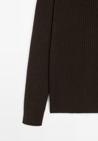 Manica di un maglione a coste di colore marrone scuro con orlo a risvolto su uno sfondo bianco, che mostra la texture e il motivo a maglia.
