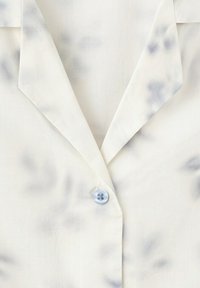 Gros plan d'un col de chemise blanc avec un unique bouton bleu clair et de subtiles taches grisâtres sur le tissu.