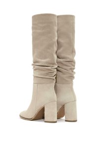 Stivali alti beige in suede con design morbido, tacchi chunky e dettaglio con zip laterale. Tessuto liscio e punta arrotondata.