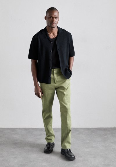 Zwarte korte mouw knopshirt, groene rechte broek, zwarte schoenen. Eenvoudig ontwerp en gladde textuur, neutrale achtergrond.