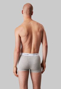 Des boxers en coton gris présentent une ceinture blanche avec le logo "Calvin Klein". La vue est prise de l'arrière, mettant en avant la texture lisse et l'ajustement.