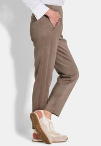 Bruine taps toelopende broeken met zijzakken, met een gladde textuur. Gecombineerd met beige sportschoenen met roze accenten en een rubberen zool.