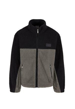 Fleeces jaka ar divkrāsu dizainu, melnas un pelēkas krāsas paneļiem, ar rāvējslēdzēju priekšā un sānu kabatām. Tekstūrēta, mīksta auduma, ar augstu apkakli.