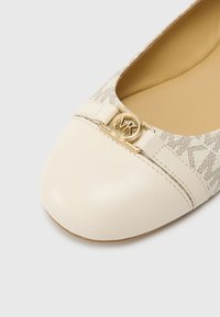 Bézs bőrből készült balerina lapos cipő kerek orral és arany logó díszítéssel. A felsőrész világos mintás textilből készült, általánosságban sima tapintású.