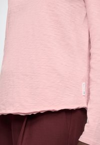 Világos rózsaszín hosszú ujjú ing enyhén texturált anyagból, lekerekített szegéllyel. Kis címke található az oldalsó varrásnál.