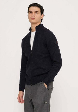 Maglione zip-up navy in un knit testurizzato, con colletto alto e polsini a coste. Accentuato da una piccola toppa con logo sulla manica.