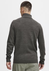 Pull en maille gris foncé avec un col haut, des poignets et un ourlet côtelés. La texture semble légèrement rugueuse, offrant une silhouette décontractée et ajustée.