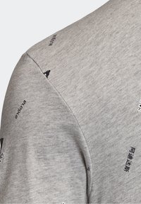 Szara bawełniana koszulka z okrągłym dekoltem, krótkimi rękawami, teksturowanym materiałem oraz nadrukowanymi czarnymi wzorami tekstowymi w okolicach ramion.