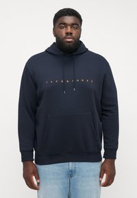 Donkerblauwe hoodie met een kangoeroezak, een capuchon met trekkoord en oranje logo tekst "JACK & JONES" over de borst. Van katoenmix stof.