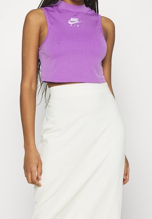 Mouwloze paarse geribbelde crop top met wit Nike Air-logo, gecombineerd met een witte rok met hoge taille, gedragen door een persoon met donker gevlochten haar.