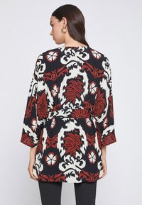 Kimono de tela negra con un audaz estampado floral en rojo y blanco, que presenta mangas de tres cuartos, cintura atada y una silueta fluida.