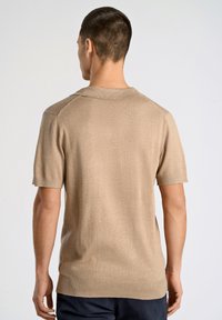 Kortärmad beige stickad pikétröja med ribbad krage, texturerat tyg och blickar i sidorna vid nederkanten. Slät finish och figurnära design.