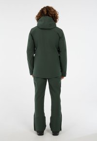 Groene waterdichte jas met een capuchon en bijpassende broek. Glad textuur, aansluitend ontwerp, ritszakken aan de zijkanten en ventilatierails bij de manchetten.