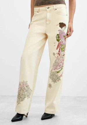 Beige vidde bukser med broderet motiv af en kvinde i lilla kimono og blomster på forsiden og nedre ben. Sorte spidse støvler er synlige.