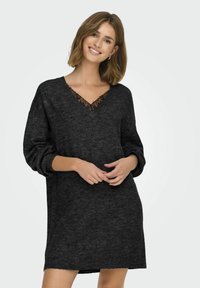 Robe noire en tricot avec un col en V, ornée de dentelle. Manches longues et amples, design décontracté. Texture douce et longueur mi-thigh.