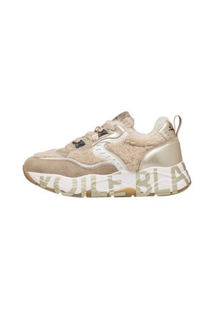 Robuster beiger Sneaker mit Lammfell-Textur, Wildleder-Paneelen, metallischen Akzenten, Schnürung vorne und markanter weißer Sohle mit teilweisem Textdesign.