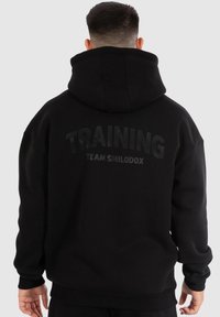 Zwarte hoodie met grote, vetgedrukte tekst "TRAINING" en "TEAM SMILODOX" op de achterkant, gemaakt van zacht, textuurstof met een capuchon.