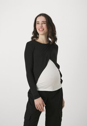 Crni longsleeve top s okruglim izrezom i omotnim dizajnom, složen preko bijele košulje, u kombinaciji s crnim cargo hlačama.