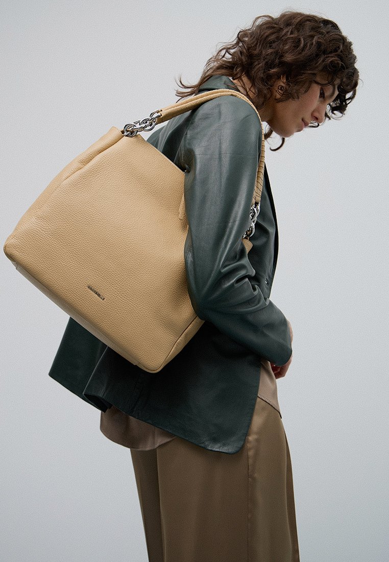 Tādas krāsas ādas rokassoma ar teksturētu apdari, kurai ir ķēdītes akcentēta siksna. Soma ir taisnstūrveida un maiga, tiek valkāta uz pleca.